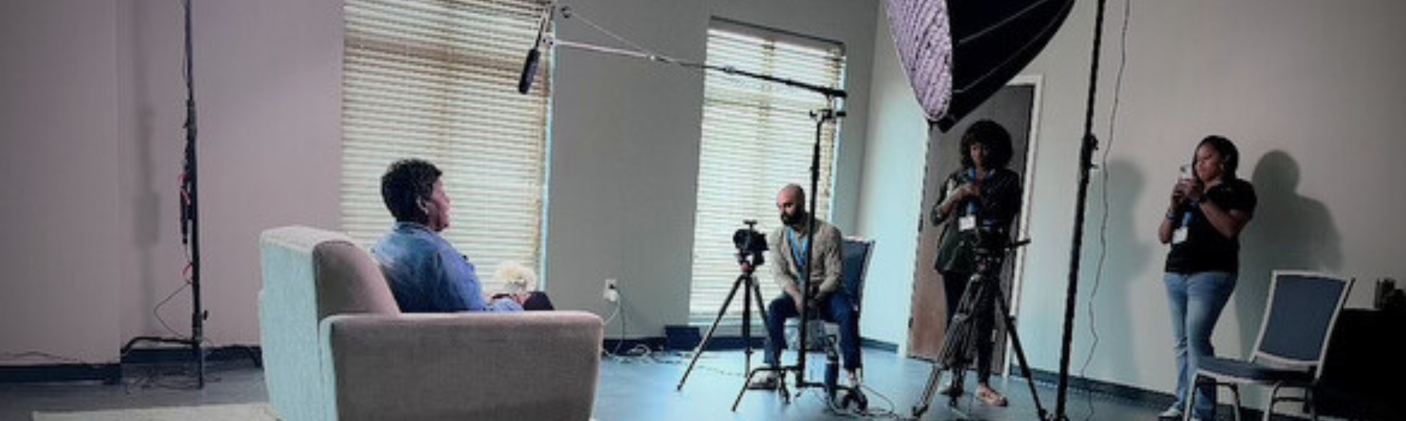 A man filming an elderly person in a bright room with large windows.